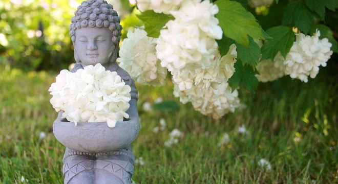 Petite statue de Buddha dans un jardin qui tient une fleur blanche