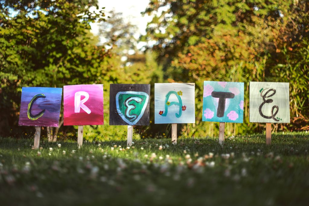 Mot anglais "create" apparait avec chaque lettre inscrite sur une pancarte colorée, apposée dans un jardin fleuri