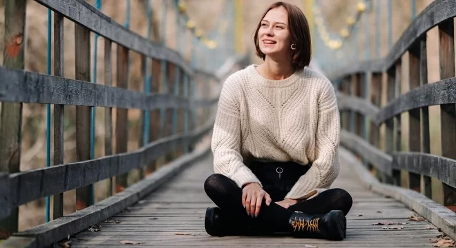 jeune femme assise en tailleur au milieu d'un pont en bois