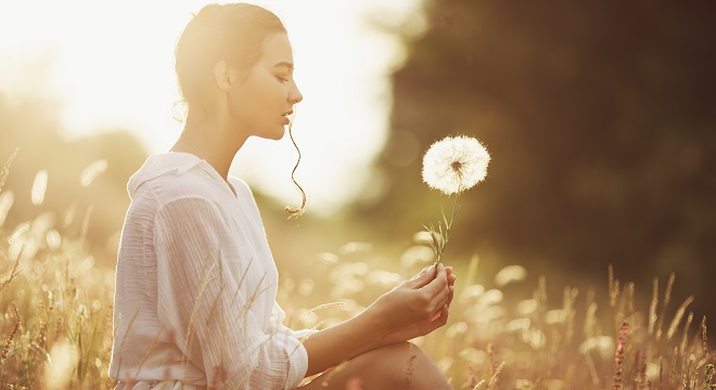 Une femme assise dans la nature qui contemple une fleur qu'elle tient dans la main