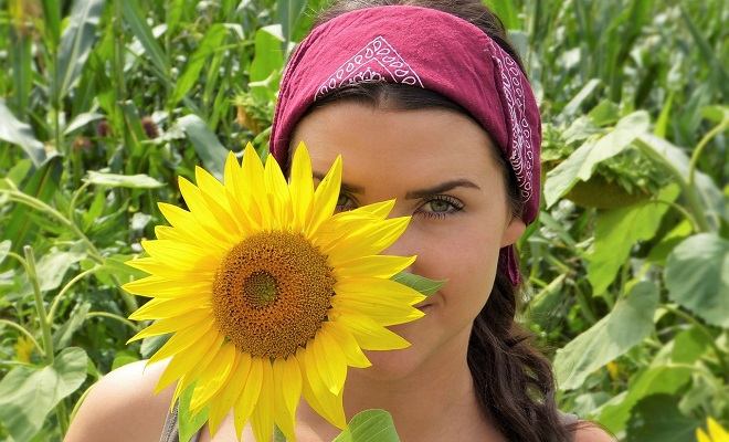 Une femme cache en partie son visage derrière une fleur de tournesol