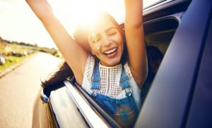 Une femme la tête et les bras levés à travers la fenêtre d'une voiture qui roule.