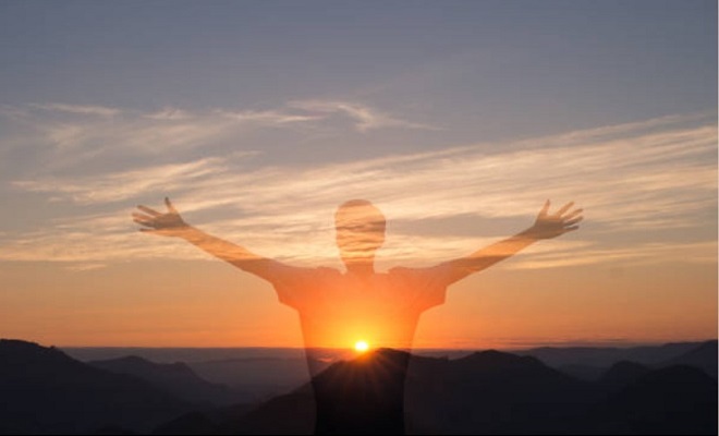 Une silhouette en transparence d'un homme écartant les bras sur fond de coucher de soleil