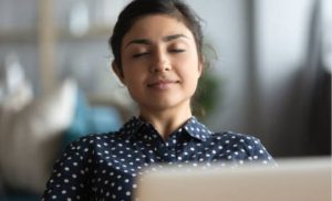 Une femme les yeux fermés devant son ordinateur esquissant un sourire serein