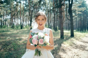 Une femme en robe de marié, qui sourit, un bouquet de fleurs à la main