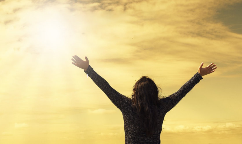 Femme qui lève les bras devant un ciel très lumineux