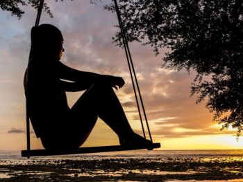 Femme, sur une balançoire, regardant la mer, au couché du soleil