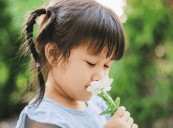 Une fillette les yeux fermés en train de sentir une fleur