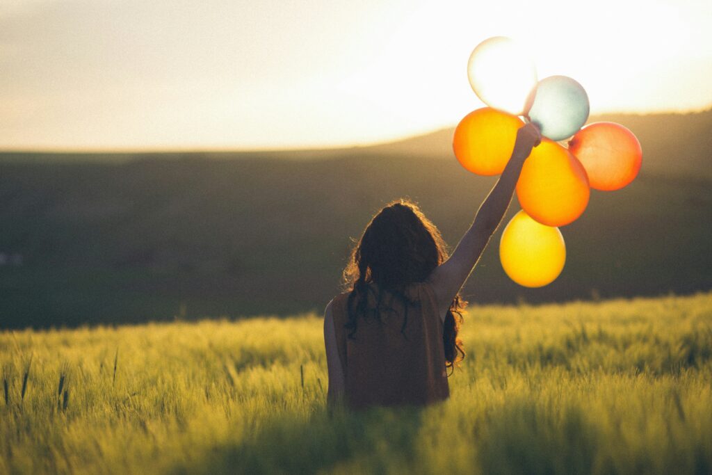 Une femme lève le bras avec des ballons colorés transparents face au soleil