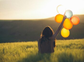 Une femme lève le bras avec des ballons colorés transparents face au soleil