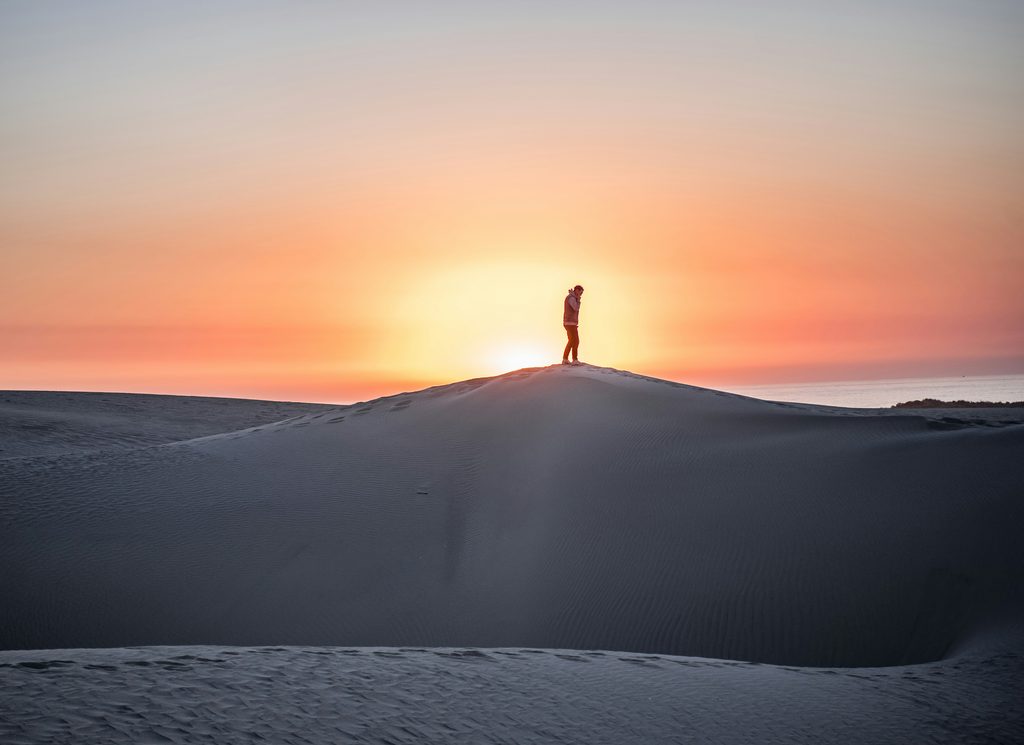 Homme debout sur une colline de sable en face d'un coucher de soleil