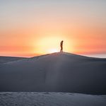 Homme debout sur une colline de sable en face d'un coucher de soleil