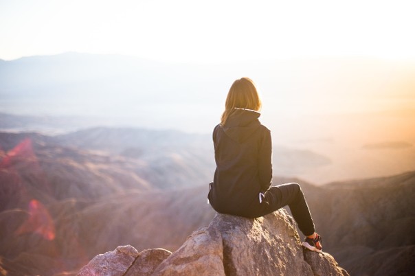 Une femme vue de dos assise sur un rocher en hauteur