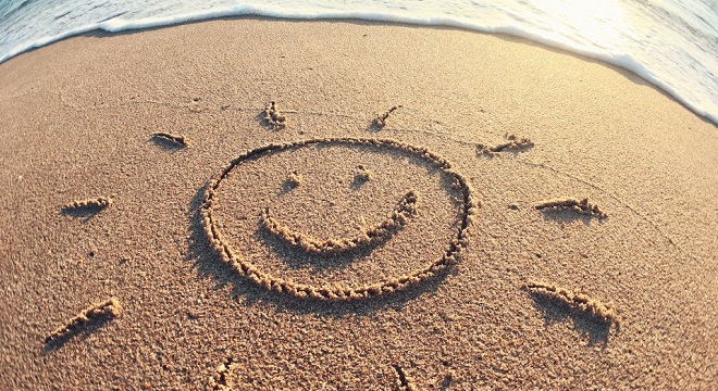 dessin sur le sable représentant un visage stylilsé rond souriant et rayonnant