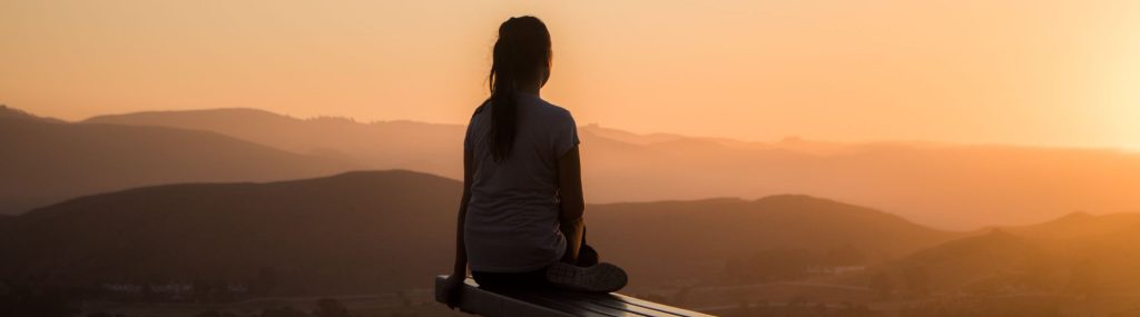 Personne en train de méditer devant un couché de soleil